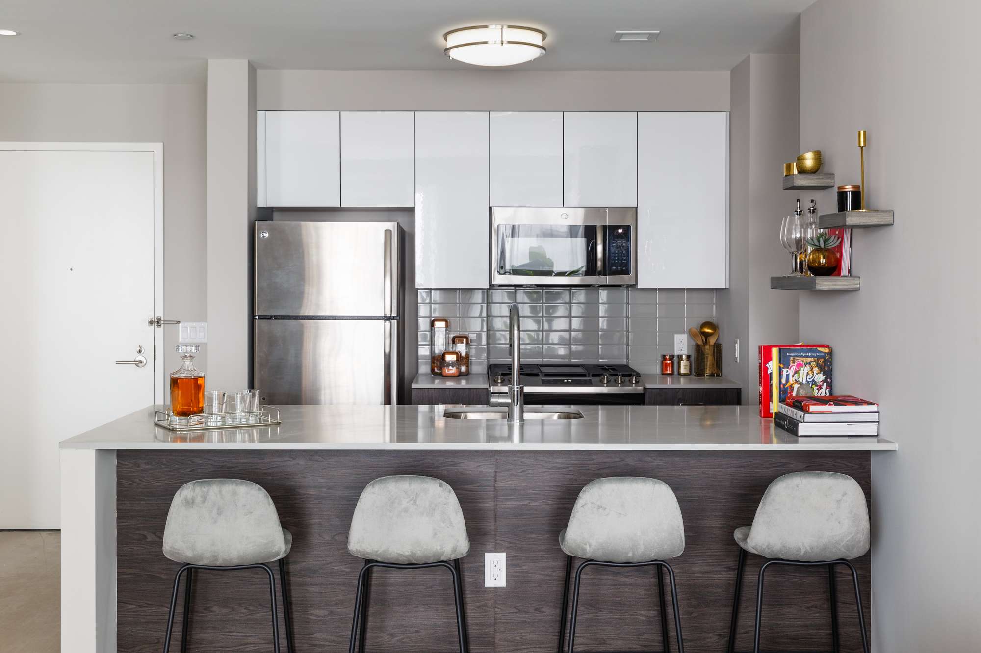 Modern galley kitchen with white cabinets, stainless steel appliances, seating counter with 4 bar stools near entrance
