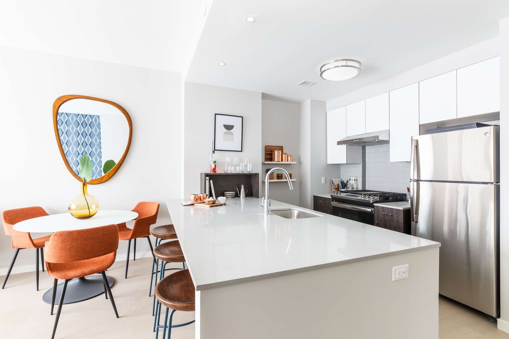 Bright, modern galley kitchen with light cabinets and large counter with bart stool seating, stainless steel appliances, and small round dining table