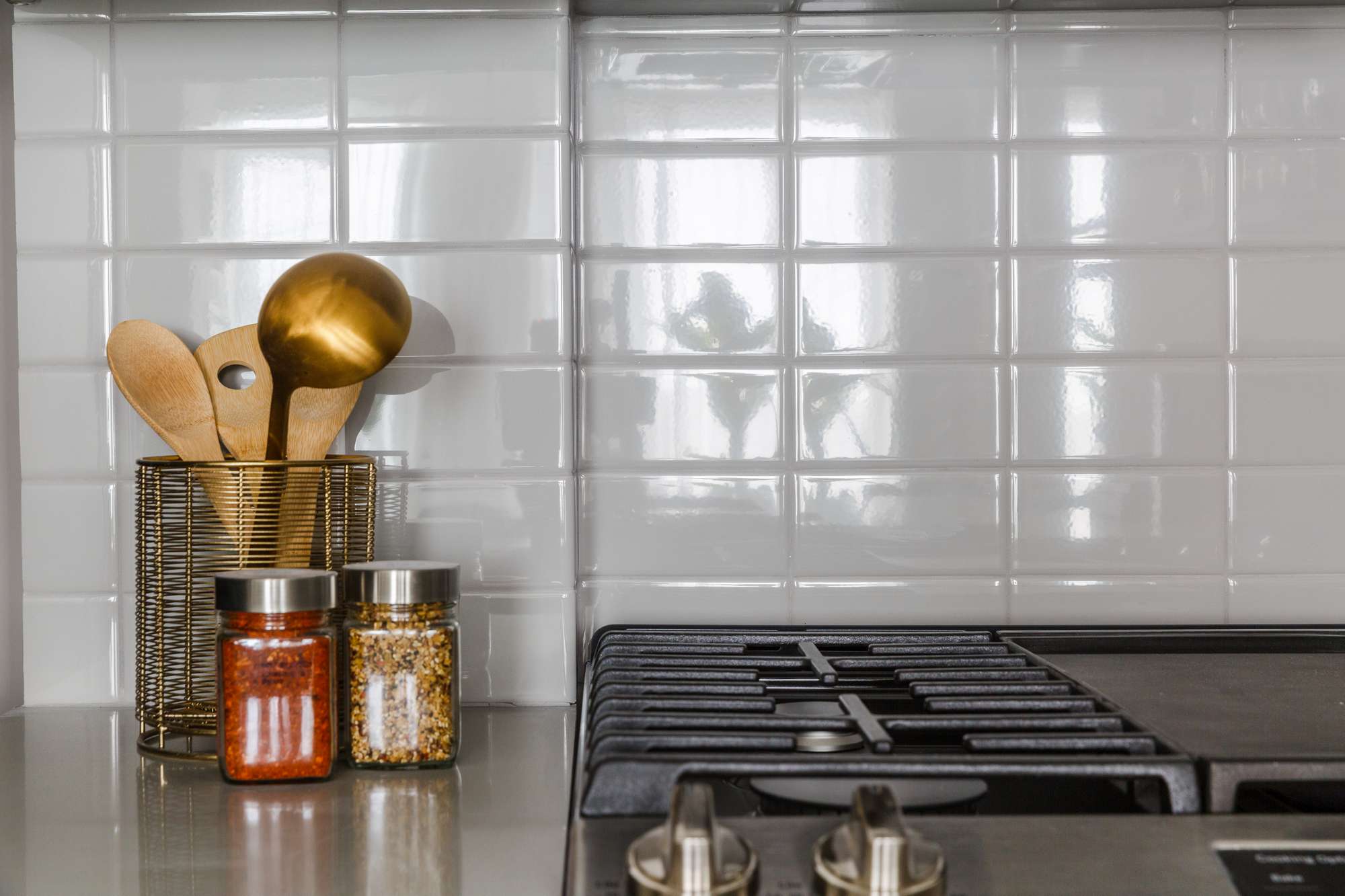 Kitchen detail of stovetop, white subway tile and counter with cooking utensils and spices